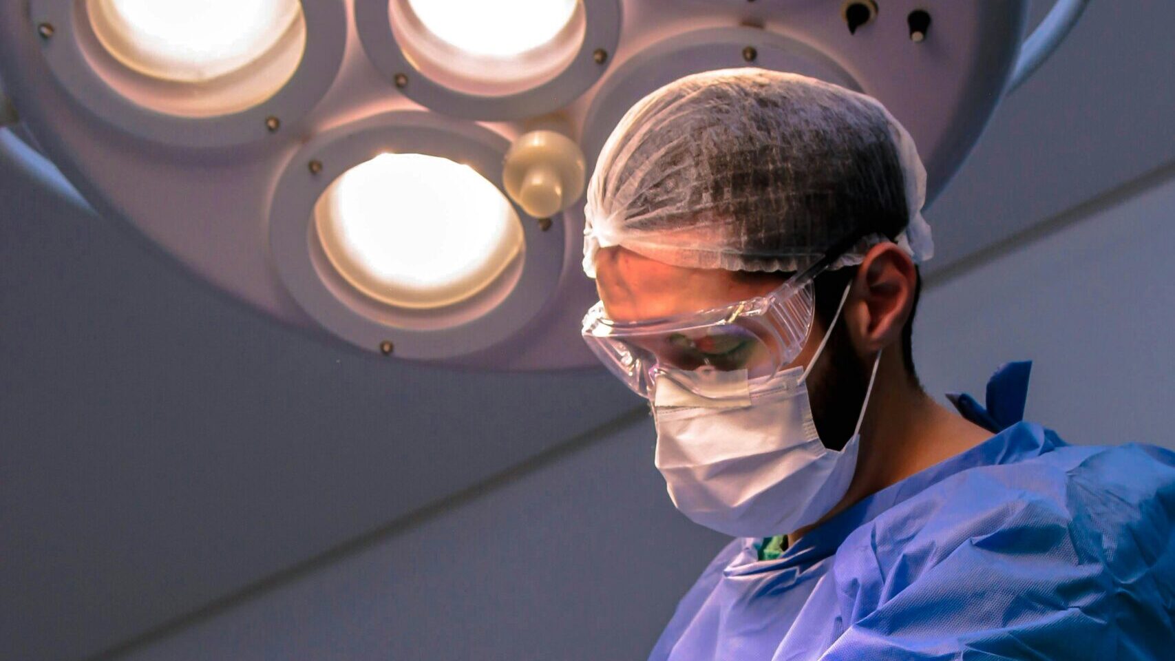 A focused surgeon in a sterile operating room performing a medical procedure under bright surgical lights.