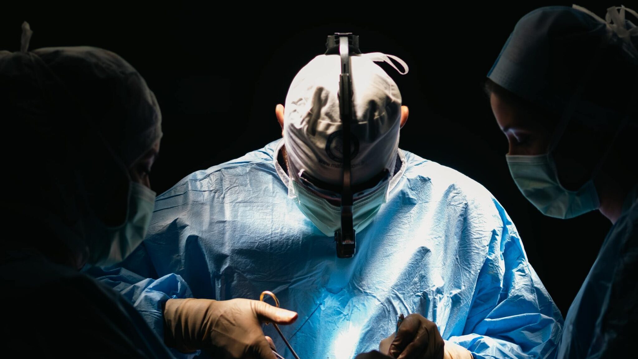 Surgeons focused in an operating room performing lifesaving surgery under bright surgical lights.
